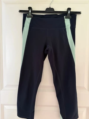 Marinblå träningsleggings med mintgrön detalj - Snygga marinblå träningsleggings med mintgröna paneler längs sidorna. Modellen är 3/4-längd och har hög midja för extra komfort. Perfekta för gymmet eller löprundan. Materialet är stretchigt och följsamt för bästa rörelsefrihet. Kolla gärna mina andra annonser❗️