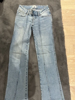 Ljusblå bootcut jeans med sömdetaljer - Säljer ett par ljusblå bootcut jeans med markerade sömmar framtill. Jeansen har klassisk femficksdesign, bälteshällor och dragkedja med knapp. Perfekta för en avslappnad och trendig look.