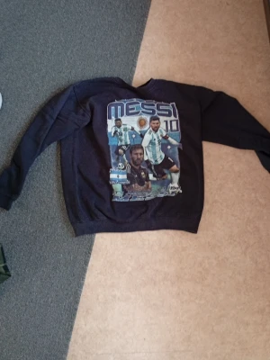 Svart sweatshirt med Messi-tryck - Cool svart sweatshirt med stort Messi-tryck på framsidan. Tröjan har rund hals, långa ärmar och ribbade muddar. Perfekt för dig som älskar fotboll och vill visa ditt stöd för Messi och Argentina.