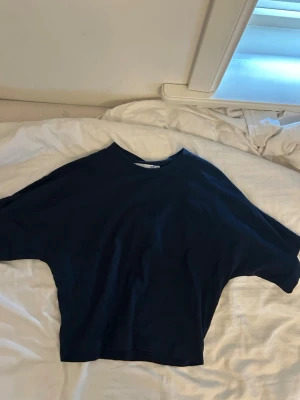Mörkblå loose topp med kort ärm - En enkel och stilren mörkblå topp med loose passform och korta ärmar. Perfekt till jeans eller kjol för en avslappnad look. Materialet känns mjukt och bekvämt, troligen bomull eller en bomullsblandning.
