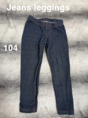Mörkblå jeansleggings stl 104 - Säljer ett par mörkblå jeansleggings i stretchigt material med fejkade sömmar och resår i midjan. Perfekta för dig som vill ha bekväma byxor med jeanslook. Passar till många olika stilar och är superenkla att matcha.🌸 Jeans leggings. Fint använt skick. Storlek 104