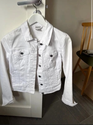 Vit jeansjacka Vero Moda XS - Snygg vit jeansjacka från Vero Moda i storlek XS. Klassisk modell med knappar framtill, två bröstfickor med lock och knapp samt raka ärmar. Perfekt att slänga över en t-shirt för en fräsch look.