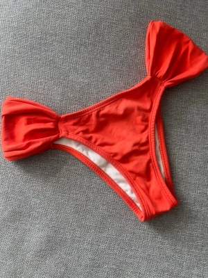 Orange  bikinitrosor med rosett från Brasilien - Snygga röda bikinitrosor från Brasilien med stora rosetter på sidorna. Modellen har en klassisk passform och är tillverkad i ett mjukt och stretchigt material som passar perfekt för strandhäng och bad. Fodrad insida för extra komfort. #bikini #brasilien 