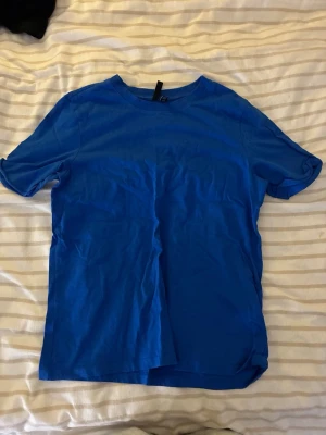 Blå basic t-shirt i bomull - En enkel blå t-shirt med rund hals och korta ärmar. Tillverkad i mjuk bomull, perfekt för en avslappnad och stilren look. Passar till det mesta och är ett måste i garderoben.