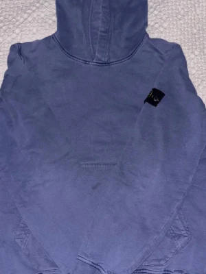 Ljuslila hoodie från Stone Island - Säljer en ljuslila hoodie från Stone Island Junior med klassisk huva och magficka. Tröjan har den ikoniska Stone Island-loggan på ärmen och är gjord i mjukt bomullsmaterial. Perfekt för dig som vill ha en stilren och bekväm hoodie.