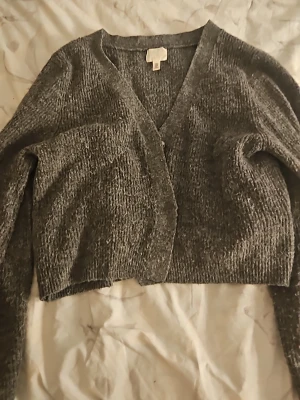 Grå cropped kofta med v-ringning - Mysig grå kofta i mjukt stickat material med v-ringning och knappstängning framtill. Croppad modell som passar perfekt till höga jeans eller kjol. Långa ärmar och enkel design gör den lätt att matcha.