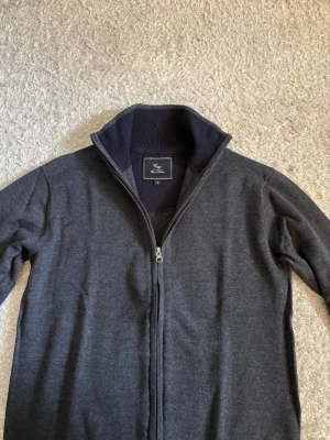 Cotti by Carl Villiam Zip Cardigan - Mörkgrå stickad cardigan från Cotti by Carl Villiam i storlek S. Dragkedja hela vägen upp och hög krage. Använd och i bra skick.  Passar lika bra till jeans som chinos och är enkel att matcha.  📦 Snabb leverans! 💬 Hör gärna av dig vid frågor eller om du vill ha fler bilder eller mått!