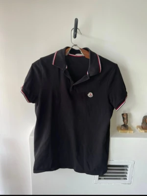 Moncler Pikétröja herr  - Säljer en svart Moncler pikétröja i storlek M.  * Original * Digitalt kvitto finns och kan visas vid intresse * Nypris: ca 2 500 kr * Fint använt skick * Klassisk modell med Moncler-logga på bröstet och röd/vit/blå detaljer på krage och ärmslut.  Skickas väl emballerad eller hämtas enligt överenskommelse.