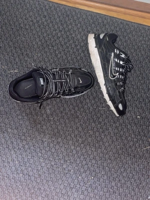 Nike P6000  - Säljer ett par svarta Nike sneakers med vita detaljer och logga på sidan. Skorna har en chunky vit sula och flera reflekterande detaljer. Ovandelen är i mesh och syntetmaterial med snörning framtill. Perfekta för dig som gillar sportig och trendig stil.