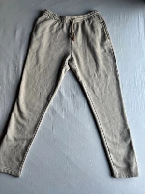 Beige mjukisbyxor från Adidas - Säljer ett par beige mjukisbyxor från Adidas med broderad logga på benet. Byxorna har dragsko i midjan och smal passform. Perfekta för chill dagar eller träning. Tillverkade i mjukt bomullsmaterial för extra komfort.