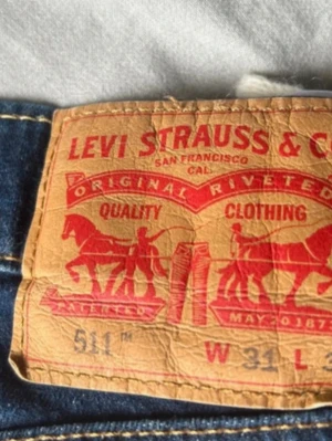 Levi's 511 blå jeans W31 - Säljer ett par klassiska blå Levi's 511 jeans med smal passform och fem fickor. Jeansen har en snygg tvätt och är tillverkade i slitstarkt denimtyg. Perfekta för dig som gillar en tidlös och stilren look.