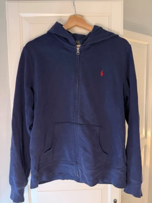 Polo ralph lauren hoodie - Storlek: jr Xl som moravarar ca XS i herratorlek. Mörkblå hoodie från Polo Ralph Lauren med dragkedja framtill och klassisk röd logga på bröstet. Tröjan har huva, två stora fickor fram och ribbade muddar vid ärmar och nederkant. Perfekt för en avslappnad och stilren look.