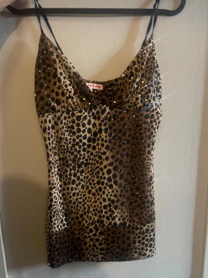 Leopardmönstrad glittrig linnetopp - Snygg leopardmönstrad linnetopp med tunna axelband och glittriga detaljer. Toppen har en v-ringad front och öppen rygg med en liten cut-out. Perfekt för dig som vill sticka ut och älskar djurmönster och glitter.