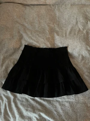 Svart volangkjol från Divided H&M - Kort svart kjol från Divided H&M med flera volanglager. Kjolen har en smockad midja och den är väldigt stretchig 🖤