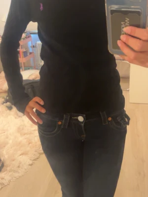 Svart långärmad topp från Ralph Lauren - Svart långärmad topp från Ralph Lauren med en liten lila logga broderad på bröstet. Toppen har en slim passform och är tillverkad i mjuk bomull, perfekt för en clean och stilren look.