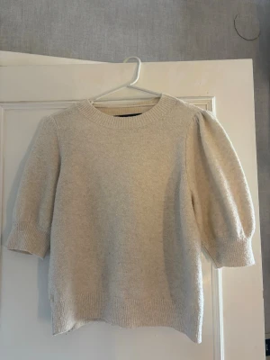 Beige stickad tröja med puffärm - Säljer en beige stickad tröja med puffärmar och ribbade muddar vid ärmslut och nederkant. Tröjan har rund halsringning och är tillverkad i ett mjukt material som känns skönt mot huden. Perfekt för dig som gillar en enkel men trendig look nu till hösten.