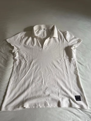 Björn Borg Piké - Klassisk vit/offwhite pikétröja från Björn Borg med en lite lösare passform samt krage och korta ärmar. Tröjan har en liten svart patch med logga längst ner. Perfekt till en clean och stilren look.