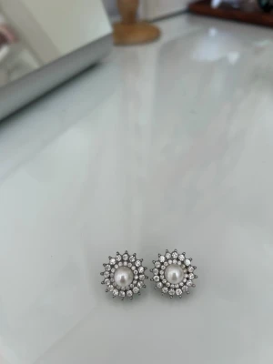 Silvriga örhängen med pärlor och stenar - Säljer ett par eleganta silvriga örhängen med rund vit pärla i mitten och gnistrande små stenar runt om. Klassisk och tidlös design som ger en lyxig känsla. 