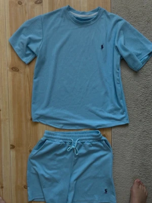 Ljusblått ribbat set från Polo Ralph Lauren - Säljer ett ljusblått ribbat set från Polo Ralph Lauren med t-shirt och shorts. Setet har en avslappnad passform, rund halsringning och dragsko i midjan på shortsen. Båda delarna har den klassiska Polo-loggan broderad framtill. Perfekt för chill dagar hemma.