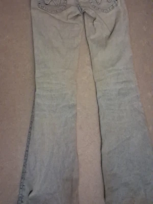 Ljusblå bootcut jeans - Säljer ett par ljusblå bootcut jeans med klassisk femficksdesign och broderade detaljer på bakfickorna. Jeansen har normal midja och är tillverkade i denim med lätt tvättad look. Perfekta för en avslappnad och trendig stil.