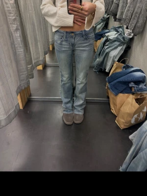 Ljusblå bootcut jeans - Säljer ett par ljusblå bootcut jeans med klassisk femficksdesign och låg midja. Jeansen har en lätt tvättad look och raka ben som går ut lite nedtill. Perfekta för en avslappnad och trendig stil.