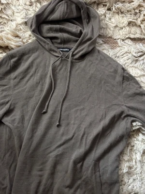 Olivgrön hoodie från J.Lindeberg - Säljer en olivgrön hoodie från J.Lindeberg med klassisk huva och dragsnören. Hoodien har en avslappnad passform och är tillverkad i mjukt bomullstyg. 