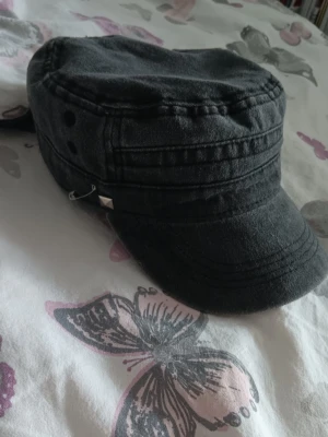 Svart armykeps - Säljer en svart armyinspirerad keps. Kepsen har en rak skärm och ventilationshål på sidorna och justerbar rem bak. Perfekt för en edgy och avslappnad stil. Har satt en säkerhetsnål och en stud på men de är enkla att ta bort om man vill. Använd några få gånger. Pris kan diskuteras 💕