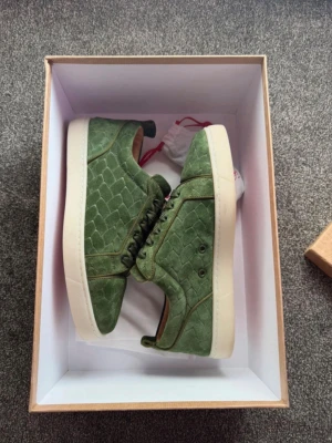 Louboutin skor - Säljer ett par gröna sneakers med unik mockaliknande struktur och mönster som påminner om fjäll. Skorna är i storlek 41 och passar till en festlig dag.💎