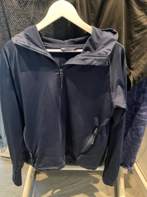 Marinblå hoodie från Marine S - Mörkblå hoodie från Marine i storlek S. Tröjan har dragkedja framtill, två fickor med dragkedja och en skön huva. Tillverkad i ett mjukt och stretchigt material som passar perfekt till chill eller träning.