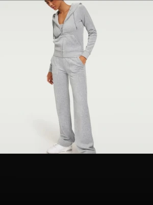 Grått mjukisset Juicy Couture  - Säljer ett grått loungewear-set med zip-hoodie och matchande byxor. Hoodien har dragkedja, fickor och ribbade muddar. Byxorna har resår i midjan och raka ben. Perfekt för chill dagar hemma eller när du vill vara bekväm.