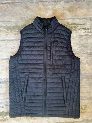 SvartJack&Jones dunväst - Snygg svart dunväst med quiltat mönster och hög krage. Västen har dragkedja framtill, två sidofickor och en bröstficka med dragkedja. Perfekt för lager-på-lager och enkel att matcha med olika outfits. Den är lite sönder där under armhålan men det syns inte så mycket när man haf på sig den, man kan se på sista bilden. 