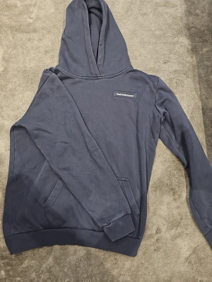 Mörkblå hoodie från Peak Performance - Snygg mörkblå hoodie från Peak Performance med klassisk logga på bröstet. Hoodien har huva, magficka och ribbade muddar vid ärmslut och nederkant. Perfekt för en avslappnad och sportig stil. Passar perfekt för dig som har storlek 170. Köpt från Intersport. Hör av dig om du har frågor😊