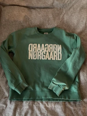 Grön sweatshirt från Nørgaard - Cool grön sweatshirt från Nørgaard med vit logga tryckt framtill. Tröjan har rund halsringning, ribbade muddar vid ärmslut och nederkant samt en relaxed passform. 💚