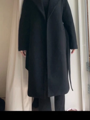 Lång höst kappa  - Fin svart lång höst kappa i strl M men passar mig som brukar ha Xs/s i kläder. För referens är jag 160. Har ytters lite ludd från stickad tröja men jag har använt klädroller. Använd kanske 5 gånger så den är i super bra skick.