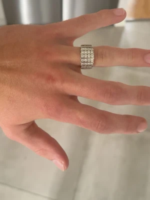 Bred 925a silverfärgad ring med stenar - Säljer en bred, silverfärgad ring med fyra rader gnistrande stenar runt hela ringen. Ringen har en stämpel på 925a på insidan. Mitt ringfingers omkrets är 6 cm