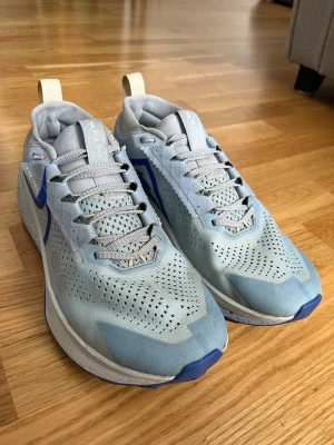 Ljusblå Nike sneakers med mesh - Snygga ljusblå sneakers från Nike med ventilerande meshmaterial och grå detaljer. Skorna har en blå swoosh på sidan, vita och grå skosnören samt vit sula med blå inslag. Perfekta för dig som gillar sportig och modern stil.