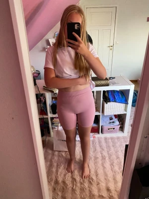 Ljusrosa cykelshorts med ribbad midja - Säljer ett par ljusrosa cykelshorts med ribbad hög midja. De är tighta och stretchiga, perfekta för träning eller chill. Materialet känns mjukt och följsamt, troligen syntet eller bomullsmix. Snygg och enkel design utan synliga loggor eller detaljer.