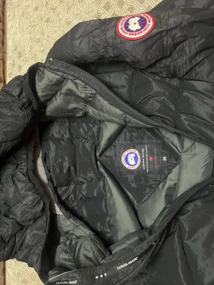Svart dunjacka  - Säljer en svart dunjacka från C’G med klassisk logga på bröstet. Jackan har quiltad design, huva och dragkedja framtill. Perfekt för kyliga dagar och riktigt snygg till alla outfits.