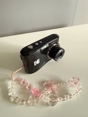 Kodak pixpro fz45 svart digitalkamera  - Säljer en svart digitalkamera från Kodak med 4x optisk zoom och bred lins. Kameran har en söt handledsrem med rosa och genomskinliga pärlor. Perfekt för dig som vill ta snygga bilder med en kompakt kamera. SD-kortplats finns.