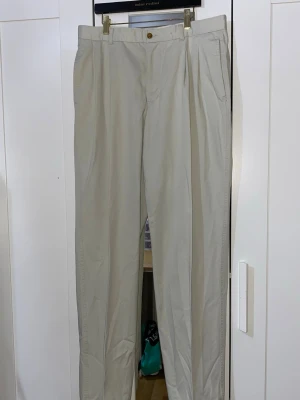 Beige chinos med pressveck - Snygga beige chinos med klassiskt pressveck och raka ben. Byxorna har fickor i sidorna och en enkel knappstängning i midjan. Perfekta för en clean och stilren look. Materialet ser ut att vara bomull eller bomullsblandning. Innerbenslängd ca 111 cm.