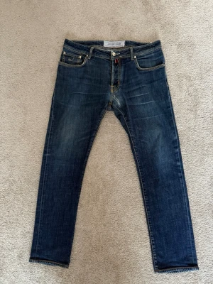 Blå jeans från Jacob Cohen - Snygga blå jeans från Jacob Cohen med klassisk femficksmodell och raka ben. Jeansen har en lätt tvättad look med subtila slitningar och kontrastsömmar. Tillverkade i mjukt denimtyg som ger en skön passform och stilren känsla.
