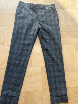 Grå rutiga kostymbyxor - Snygga grå kostymbyxor med diskret rutmönster och raka ben. Byxorna har bälteshällor, sidofickor och en bakficka med knapp. Perfekta för en stilren look och passar till skjorta eller t-shirt.       Storlek 30/30.                                                              Pris kan diskuteras 