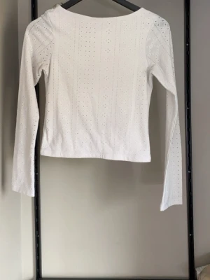 Vit långärmad topp med hålmönster - Säljer en vit långärmad topp med hålmönster i hela tyget. Toppen har en rund halsringning och är tillverkad i ett mjukt material som känns bekvämt mot huden. 