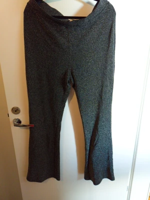 Glittriga svarta bootcut leggings - Säljer ett par svarta leggings med glittereffekt och bootcut-ben. Materialet är stretchigt och skimrar snyggt i ljuset, perfekta för dig som vill sticka ut lite extra. Resår i midjan för skön passform.