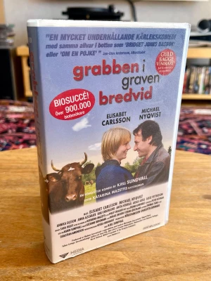 FABRIKSNY / INPLASTAD! Grabben i graven bredvid (VHS) – Ovanlig samlarfilm! - Helt unik chans för nostalgikern eller VHS-samlaren! En helt ny, oöppnad och fabriksinplastad köpfilm på VHS med den svenska succékomedin ”Grabben i graven bredvid” från 2002. Extremt svårt att hitta svensk 2000-talsfilm i detta orörda skick idag!