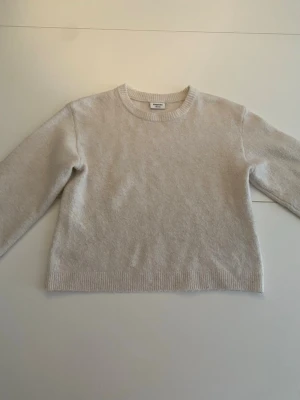 Beige stickad tröja med rund hals - En enkel och stilren beige stickad tröja med rund halsringning och långa ärmar. Tröjan har ribbade muddar vid ärmslut och nederkant, vilket ger en klassisk look. Perfekt att matcha med jeans eller kjol för en avslappnad stil.Den är ifrån Kappahl och är i storlek 146-152