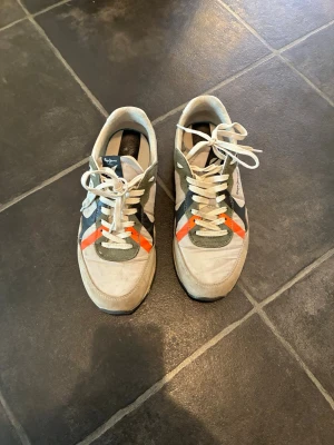 Sneakers med beige och orange detaljer - Snygga sneakers från Pepe Jeans i beige mocka och textil med gröna och orange detaljer. Skorna har vita snören och en klassisk låg siluett som passar till många olika stilar. Sula i gummi och logga på sidan.
