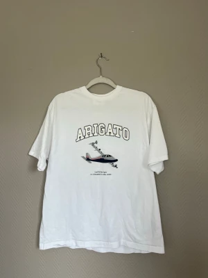 Vit t-shirt från Axel Arigato - Säljer en vit t-shirt från Axel Arigato med tryck av ett flygplan och texten 'ARIGATO' på bröstet. Klassisk rund hals och korta ärmar. 