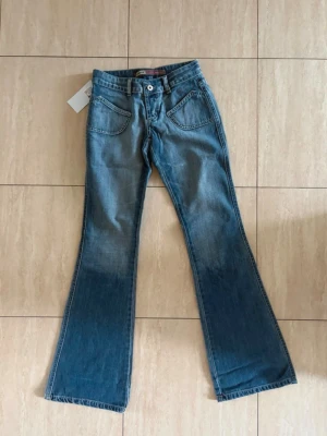 Blå bootcut jeans med utsvängda ben - Säljer ett par blå bootcut jeans med utsvängda ben och klassiska femficksdetaljer. Jeansen har en snygg tvätt med ljusare partier upptill och mörkare nedtill. Tillverkade i denim med normal midja och bälteshällor. Perfekta för en trendig och avslappnad look.