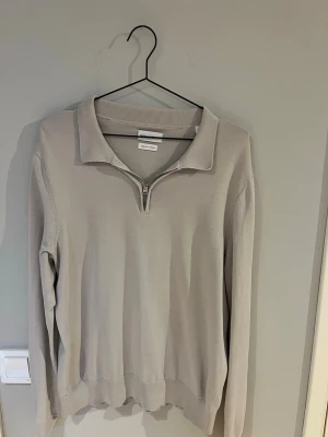 Ljusgrå halvzip tröja These Glory Days - Snygg ljusgrå tröja från These Glory Days med halvzip och krage. Tillverkad i mjuk superior cotton som känns riktigt skön mot huden. Perfekt för dig som gillar stilrena och enkla plagg med en modern touch. Långa ärmar och ribbade muddar.